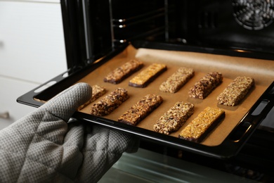 Photo of Woman taking delicious healthy granola bars from oven, closeup