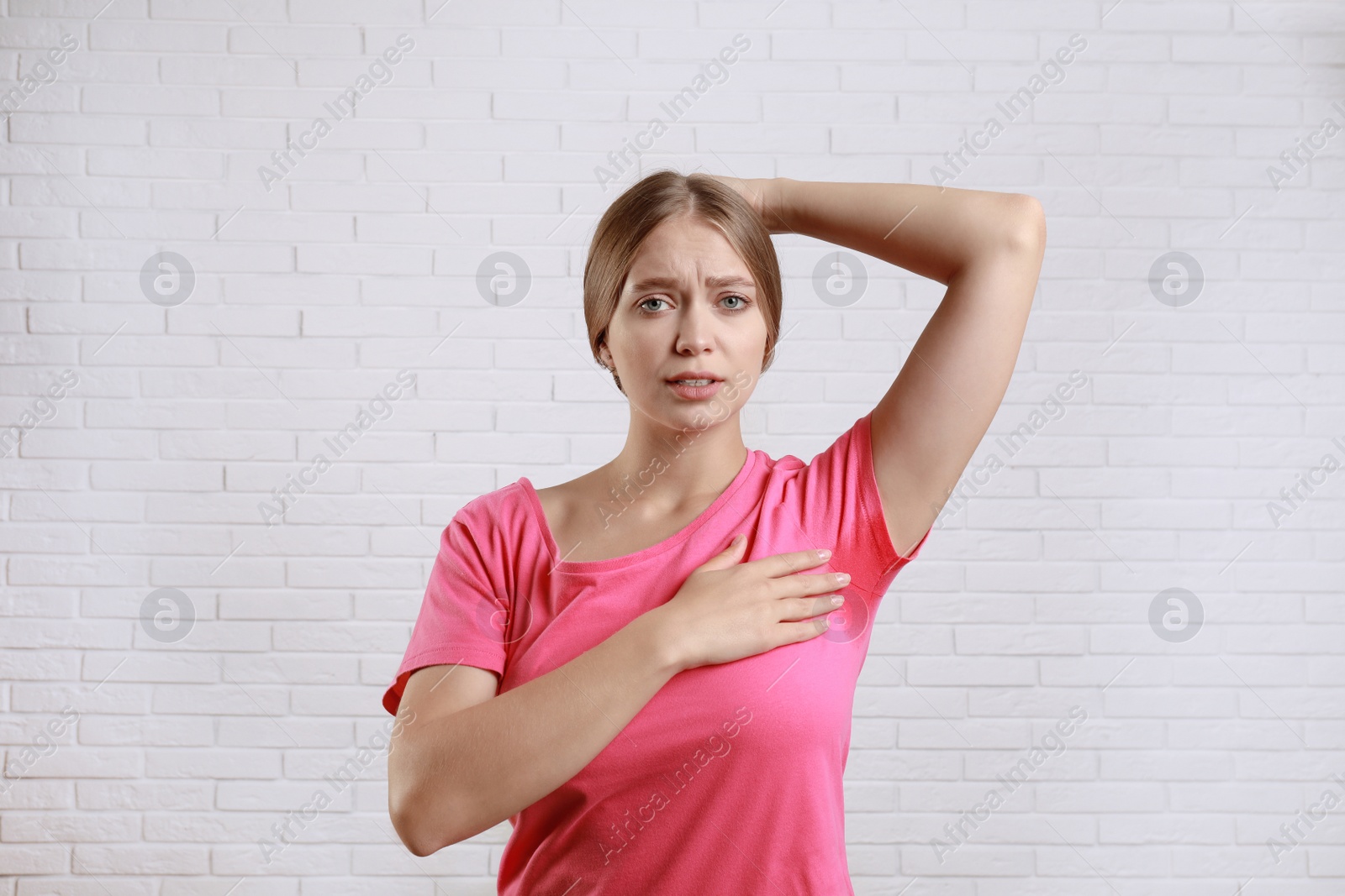 Photo of Young woman with sweat stain on her clothes against brick wall. Using deodorant