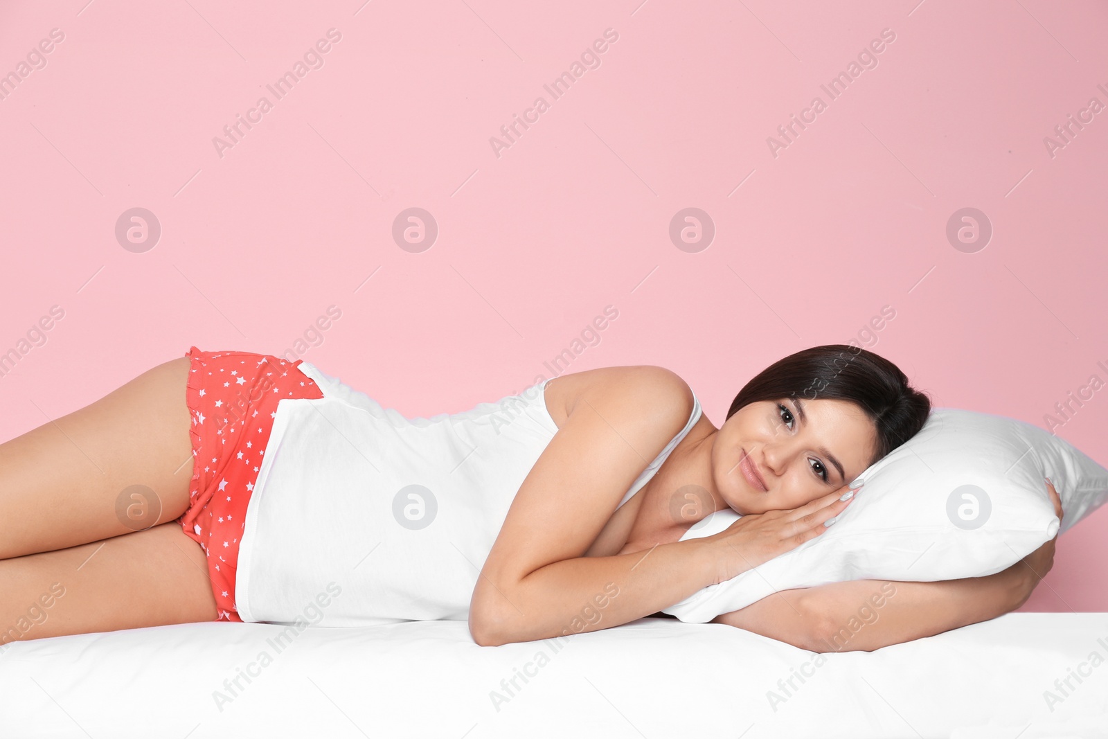 Photo of Beautiful woman lying with comfortable pillow on bed against color background