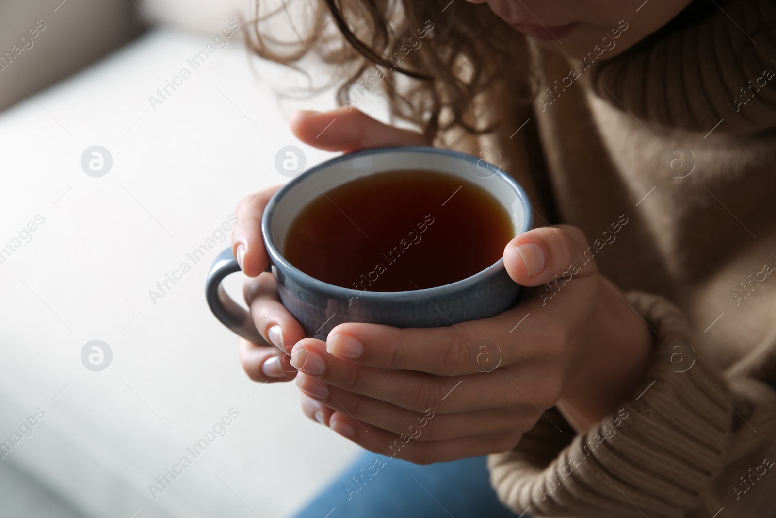 Photo of Woman with cup of hot tea indoors, closeup. Cozy home atmosphere