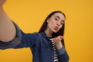 Young woman taking selfie and blowing kiss on yellow background