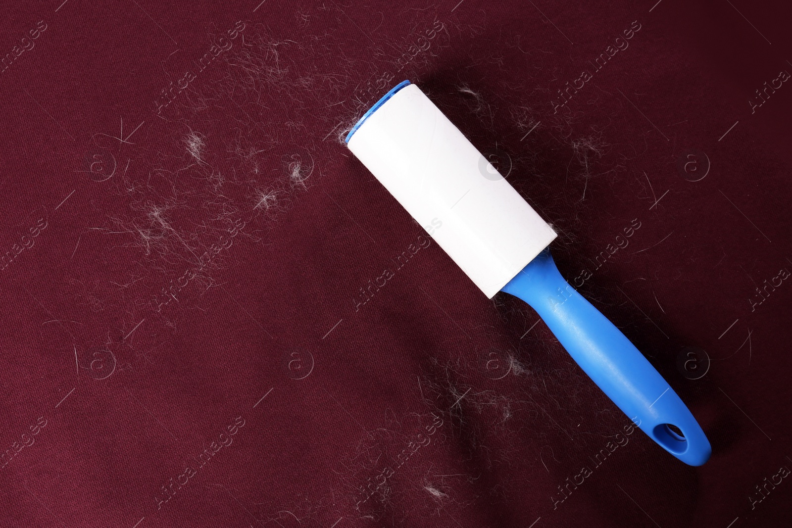 Photo of Lint roller on red fabric covered with hair, top view. Space for text