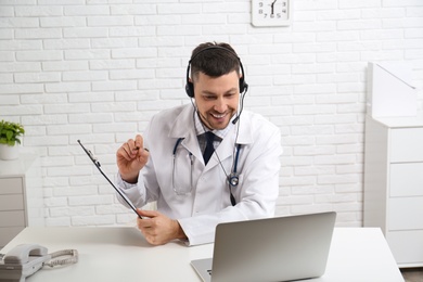 Doctor with headset consulting patient online at desk in clinic. Health service hotline