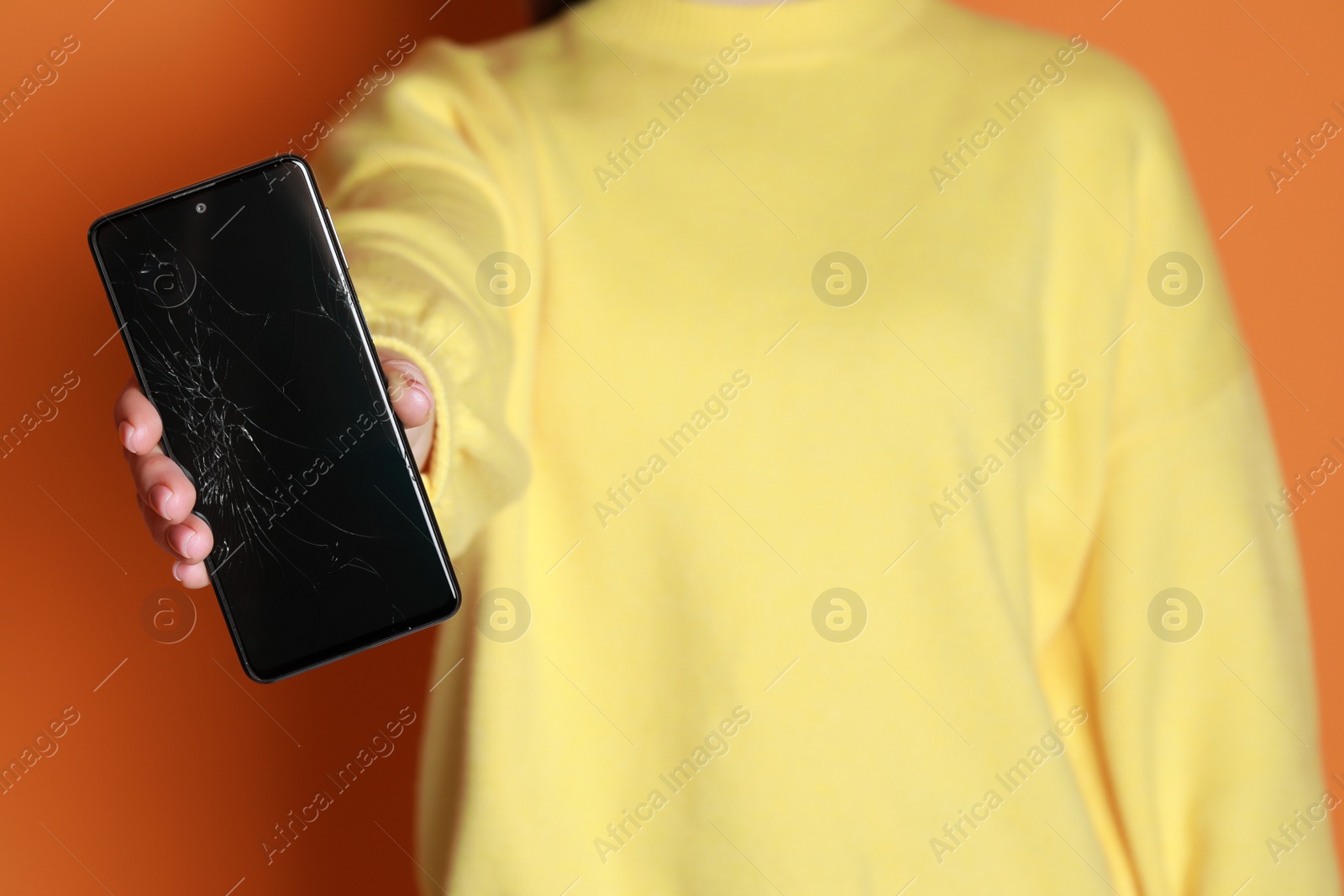 Photo of Woman showing damaged smartphone on orange background, closeup. Device repairing