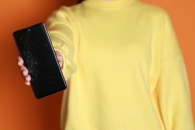 Woman showing damaged smartphone on orange background, closeup. Device repairing