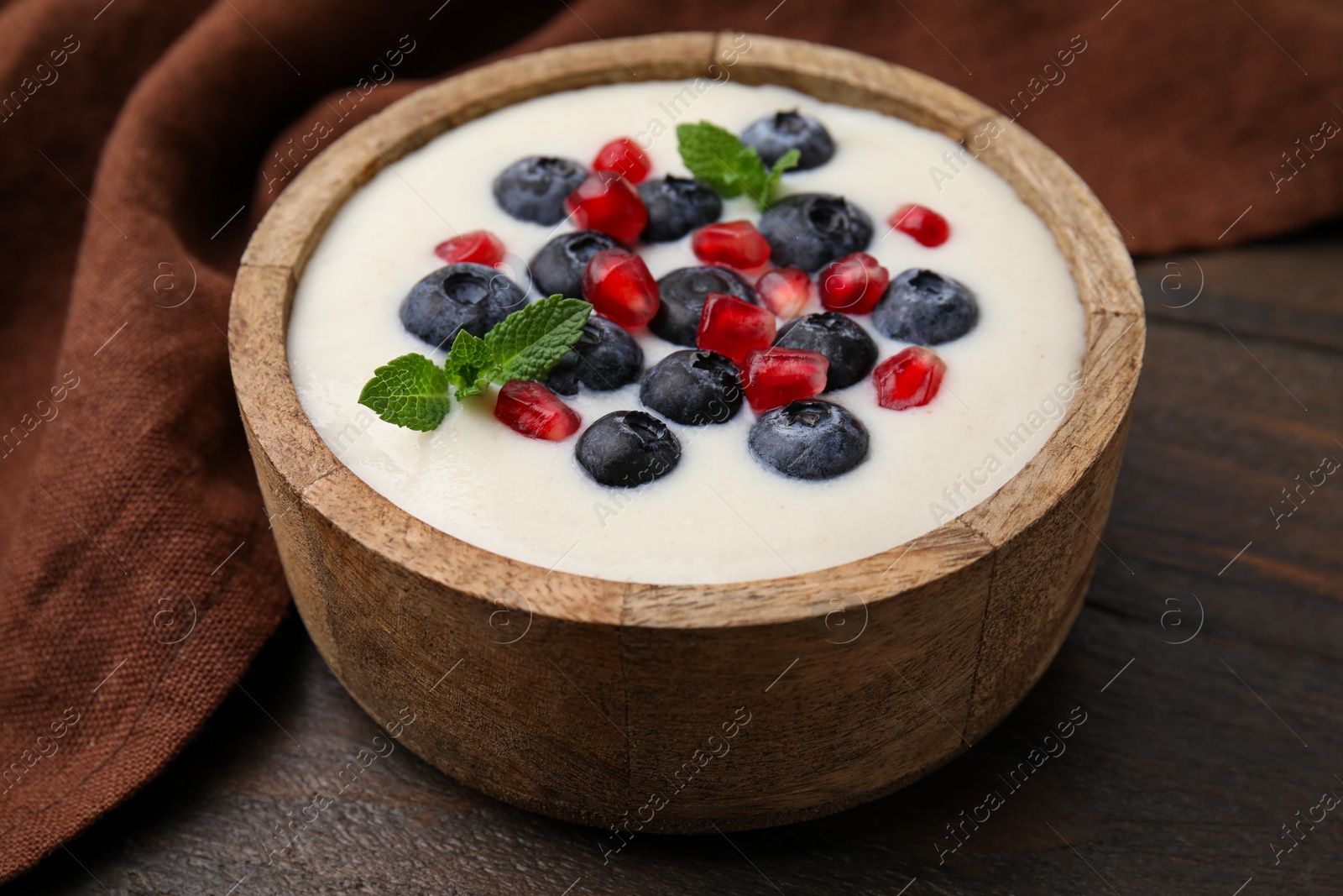 Photo of Bowl of delicious semolina pudding with blueberries, pomegranate and mint on wooden table, closeup