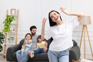 Happy family having fun at home. Mother dancing while her relatives resting on sofa