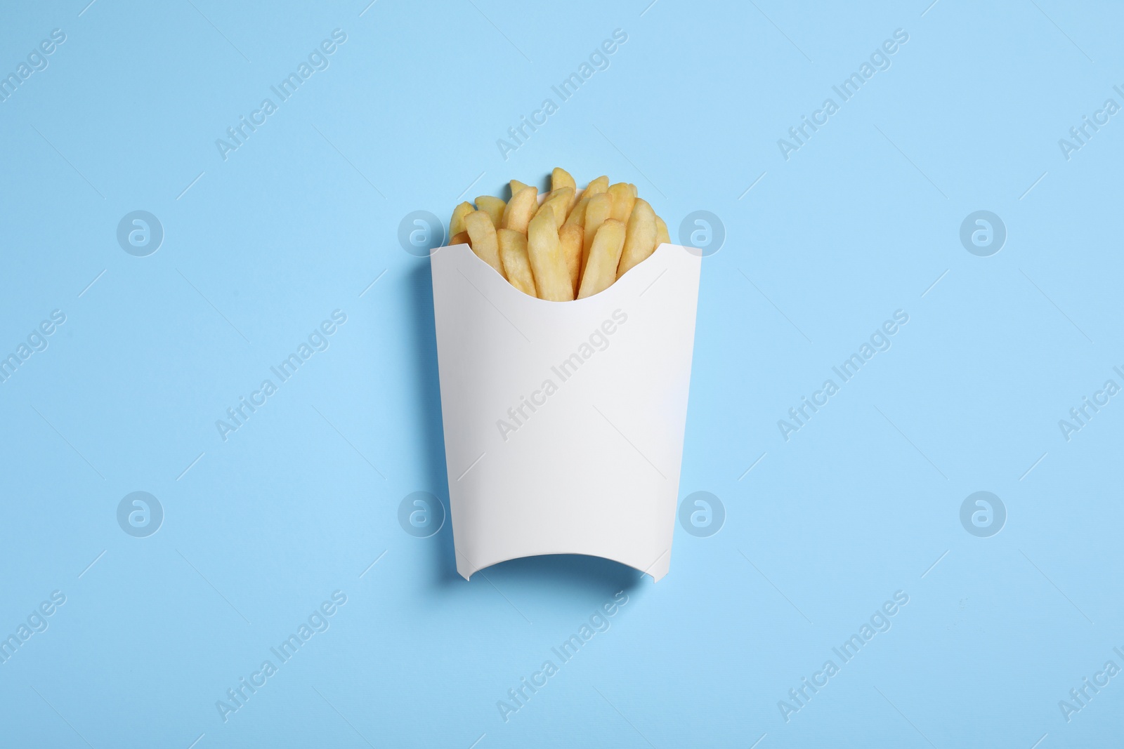 Photo of Paper cup with French fries on light blue table, top view