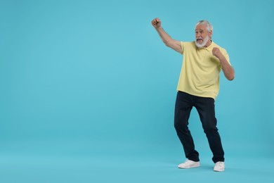 Emotional senior sports fan celebrating on light blue background, space for text