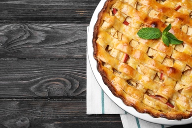 Photo of Traditional apple pie with mint on black wooden table, top view. Space for text
