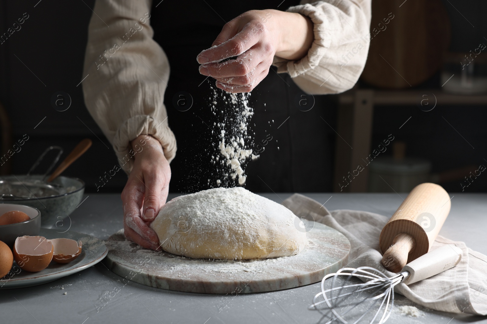 Photo of Making dough. Woman adding flour at grey table, closeup