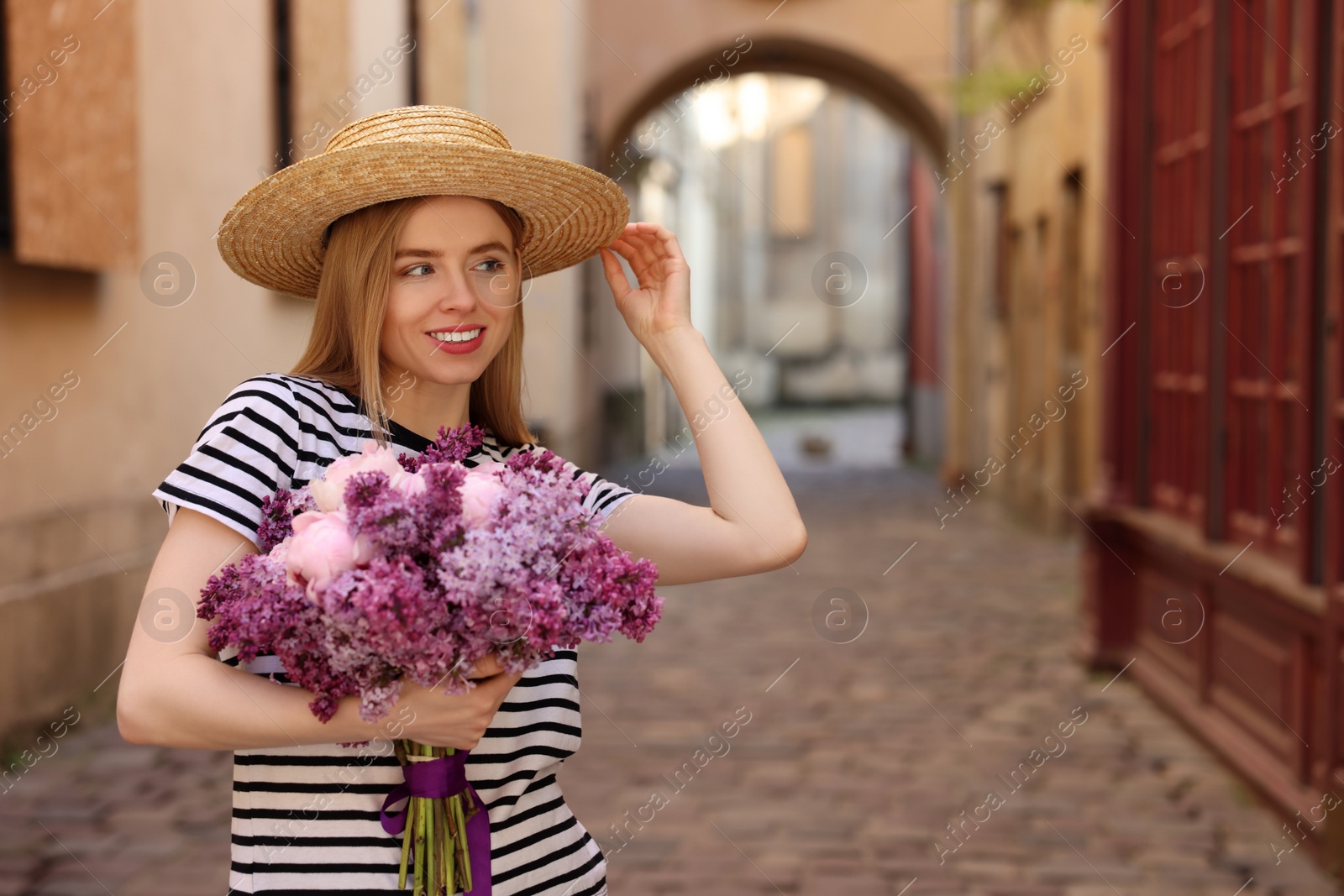 Photo of Beautiful woman with bouquet of spring flowers on city street, space for text