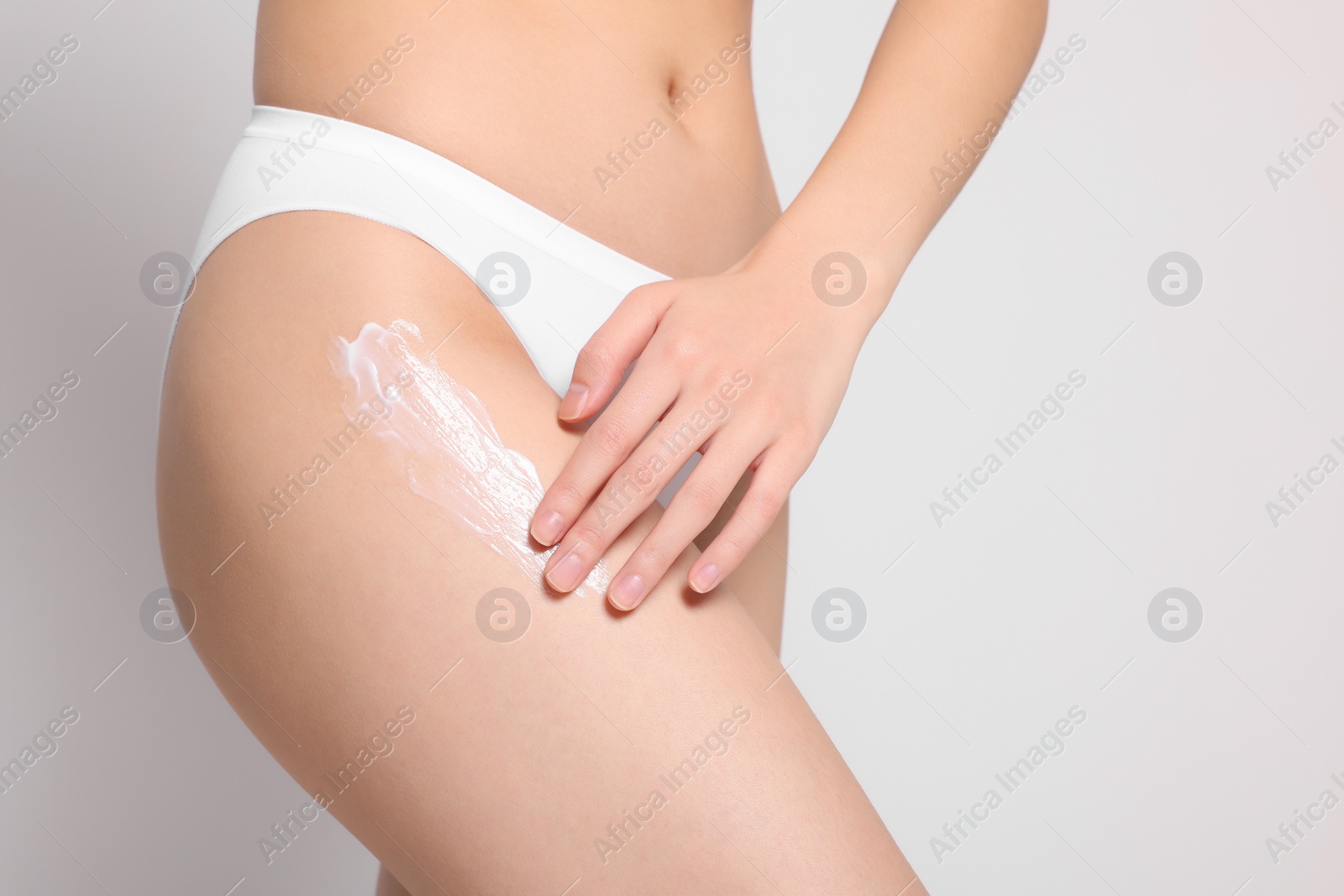 Photo of Woman applying body cream onto hip on light grey background, closeup. Space for text