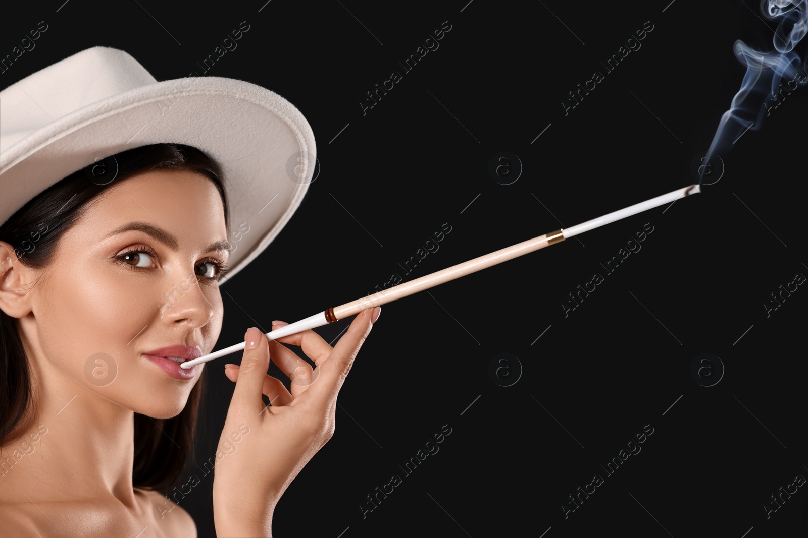 Photo of Woman using long cigarette holder for smoking on black background