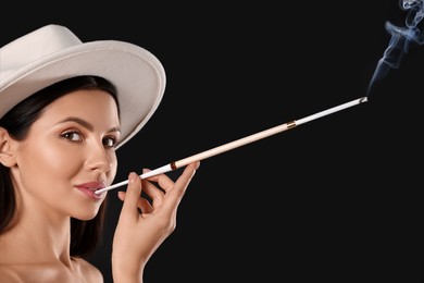 Woman using long cigarette holder for smoking on black background