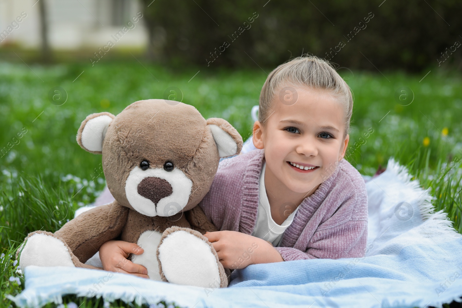 Photo of Little girl with teddy bear on plaid outdoors