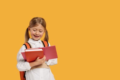 Happy schoolgirl with backpack and books on orange background, space for text