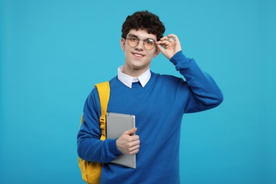 Portrait of student with backpack and tablet on light blue background