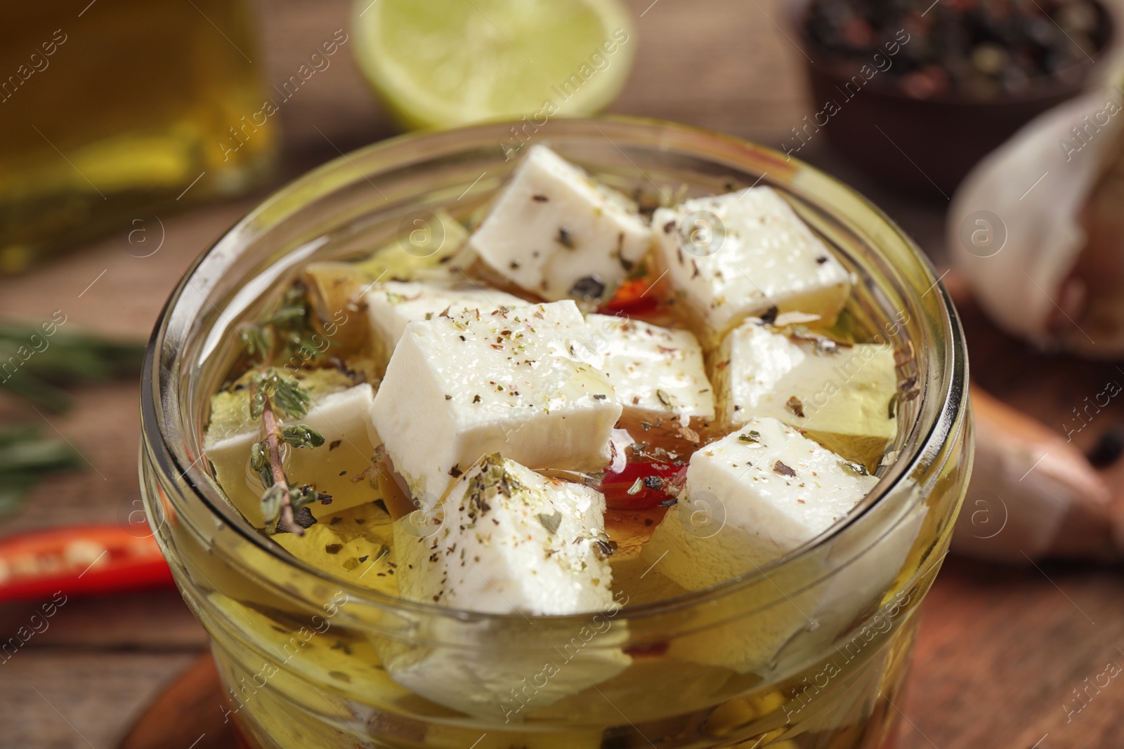 Photo of Glass jar of marinated feta cheese on wooden table, closeup