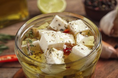 Glass jar of marinated feta cheese on wooden table, closeup