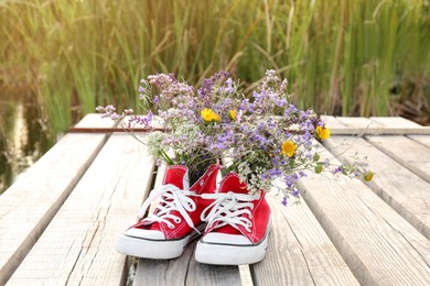 Photo of Shoes with beautiful flowers on deck outdoors