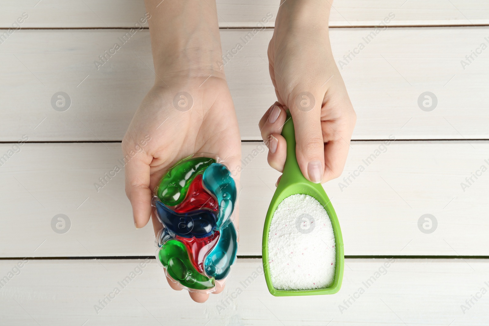 Photo of Woman holding laundry capsules and detergent powder above white wooden table, top view