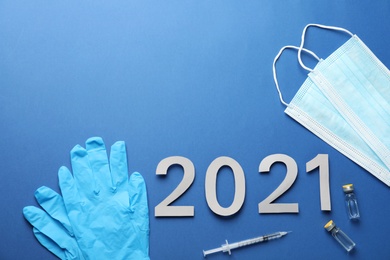 Photo of Flat lay composition with coronavirus vaccine and number 2021 on blue background. Space for text