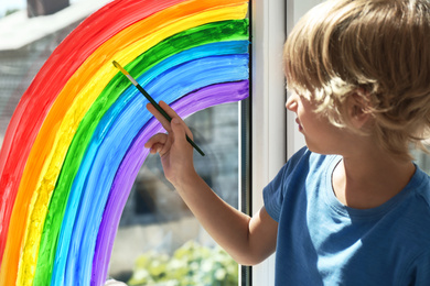 Photo of Little boy drawing rainbow on window indoors. Stay at home concept