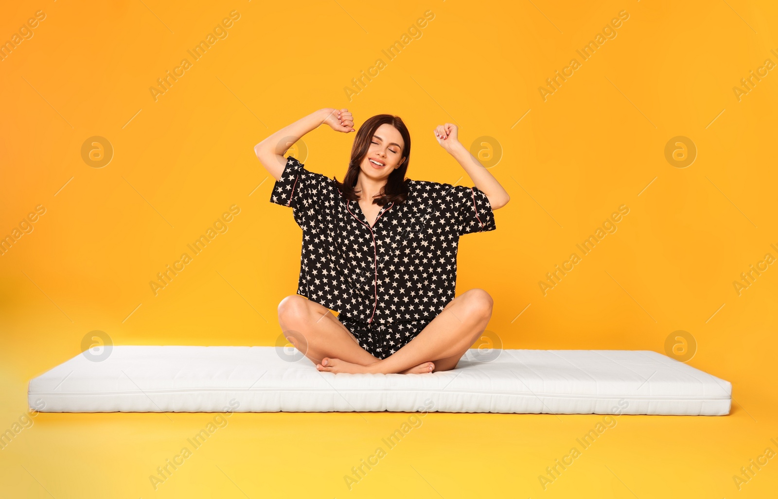 Photo of Young woman stretching on soft mattress against orange background