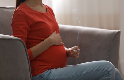 Photo of Young pregnant woman smoking cigarette at home, closeup. Space for text