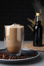 Photo of Glass of coffee with syrup and beans on light grey table