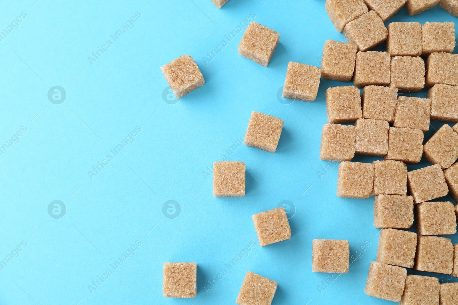 Photo of Brown sugar cubes on light blue background, top view. Space for text