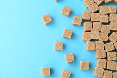 Photo of Brown sugar cubes on light blue background, top view. Space for text