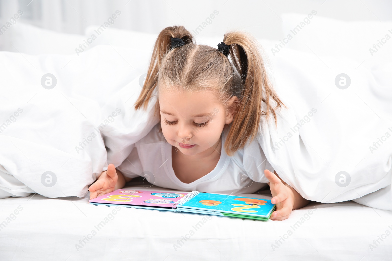 Photo of Beautiful little girl with book in bed at home. Bedtime schedule