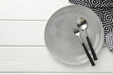 Stylish setting with cutlery, napkin and plate on white wooden table, top view. Space for text