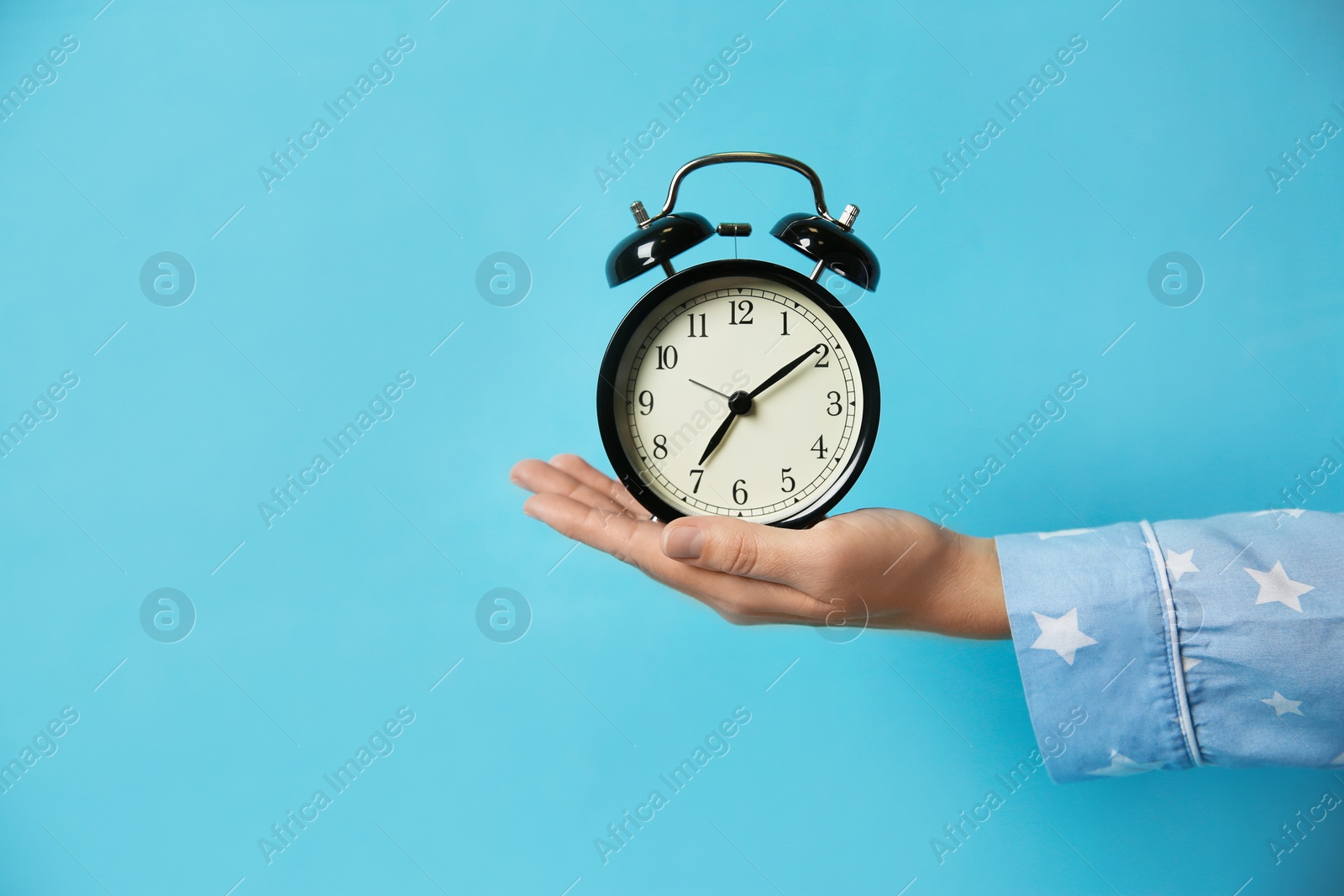 Photo of Woman holding alarm clock on light blue background, closeup. Morning time