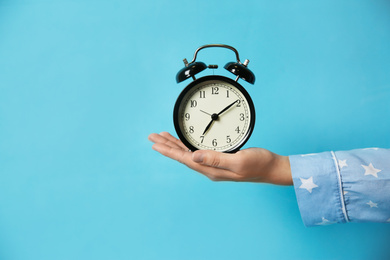 Photo of Woman holding alarm clock on light blue background, closeup. Morning time