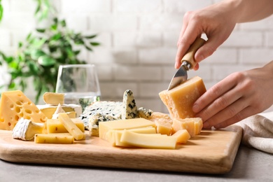 Photo of Woman cutting parmesan for cheese plate at table, closeup
