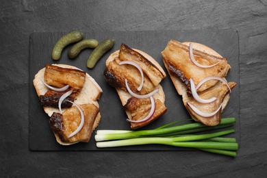 Photo of Tasty fried pork lard with bread slices and onion on black table, top view