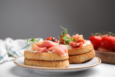 Photo of Tasty rusks with prosciutto, cream cheese and tomatoes served on white table