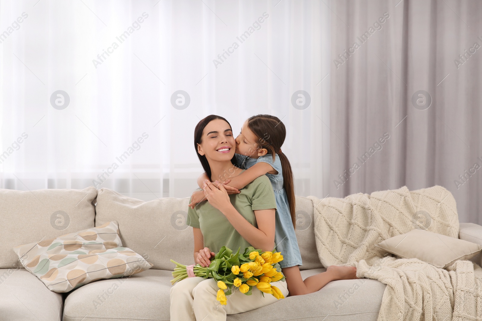 Photo of Happy woman and her cute daughter with bouquet of yellow tulips on sofa at home. Mother's day celebration