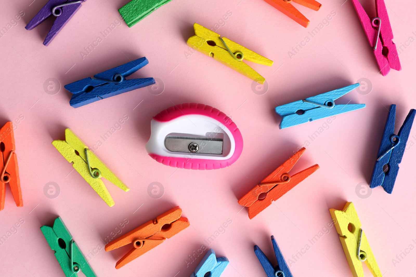 Photo of Colorful clothespins and sharpener on pink background, flat lay. Diversity concept