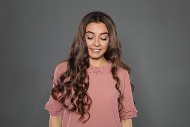 Beautiful woman with shiny wavy hair on grey background