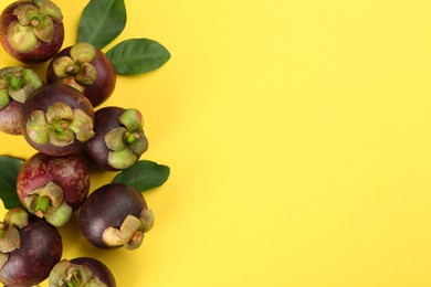 Photo of Fresh ripe mangosteen fruits with green leaves on yellow background, flat lay. Space for text