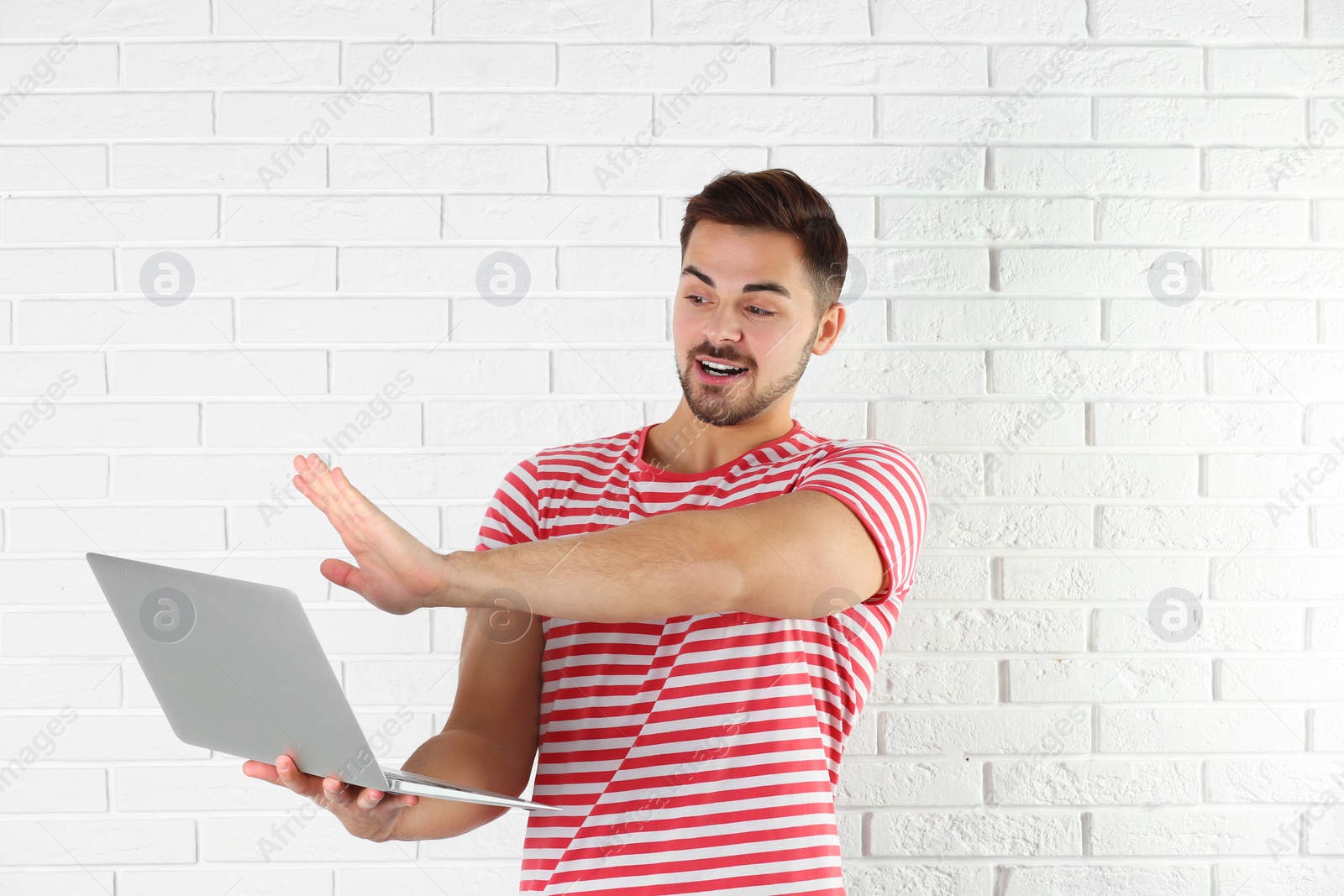 Photo of Man using laptop for video chat against brick wall