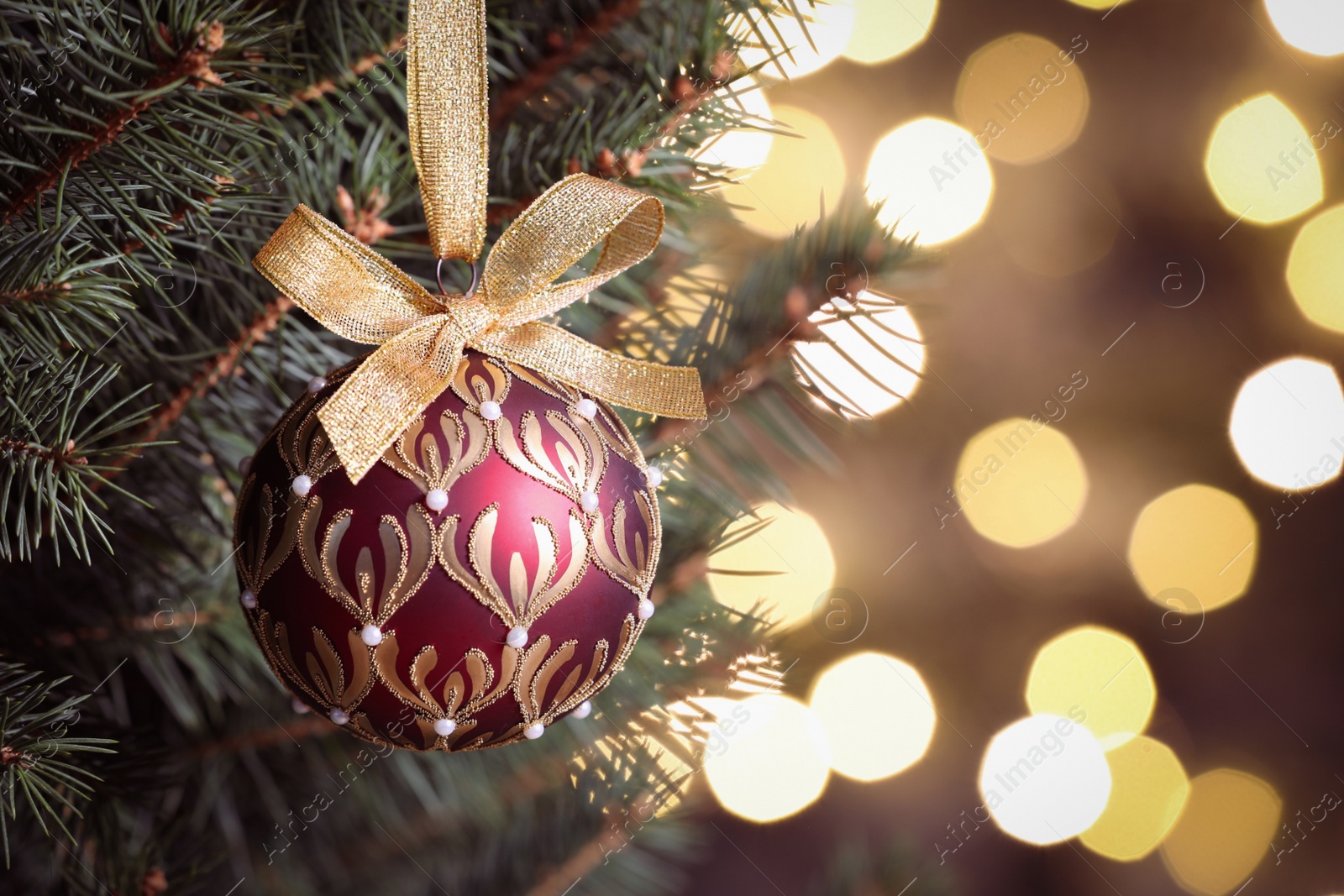 Photo of Shiny red ball hanging on Christmas tree against festive lights, closeup. Space for text