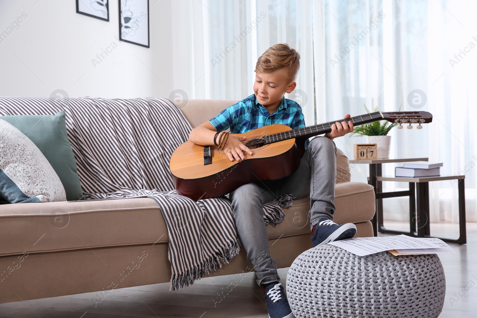 Photo of Cute little boy playing guitar on sofa in room