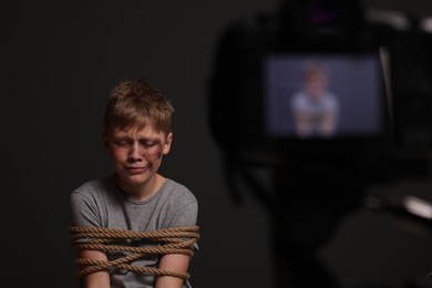 Little boy with bruises tied up and taken hostage near camera on dark background, selective focus
