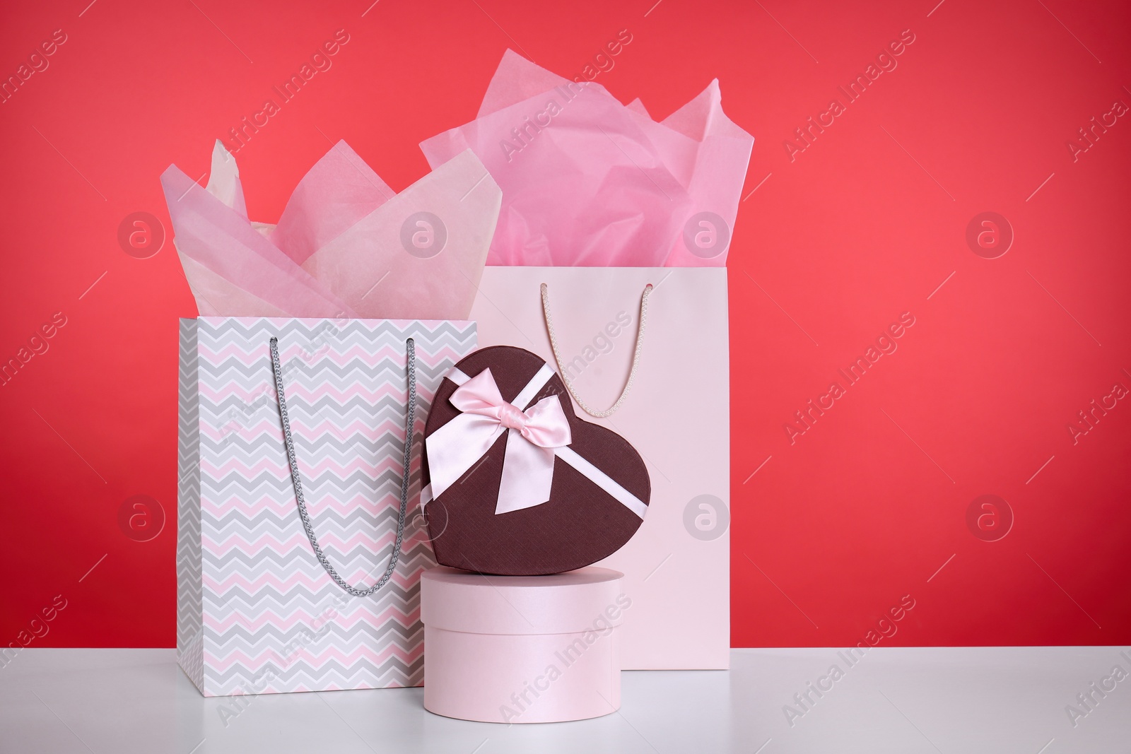 Photo of Shopping paper bags and gift boxes on red background. Space for text