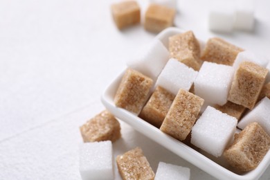 Photo of Different sugar cubes in bowl on white table, closeup. Space for text